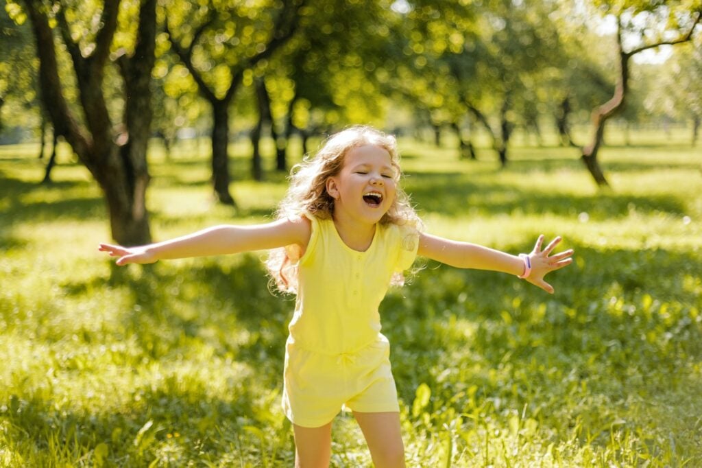 A happy foster child playing in a summer park. The girl is running, spinning, spinning and laughing